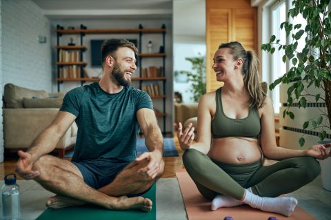 Giovane donna incinta che pratica yoga con il marito a casa.